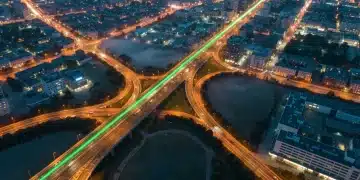 Vue aérienne d'un réseau urbain complexe au lever du soleil avec des routes éclairées, symbolisant les parcours clients omnicanal fluides et interconnectés. Une ligne verte symbolise l'intégration.